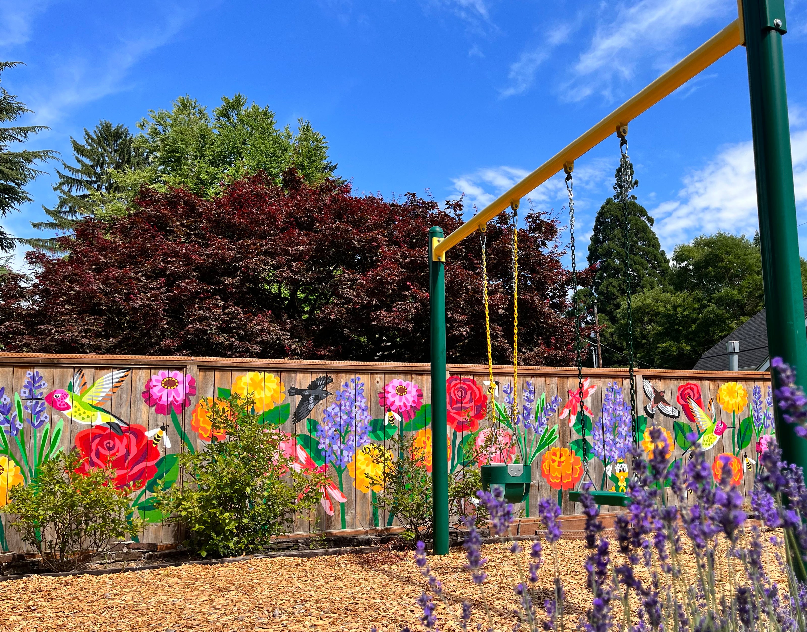 Color flowers painted on a fence in front of a swing set 