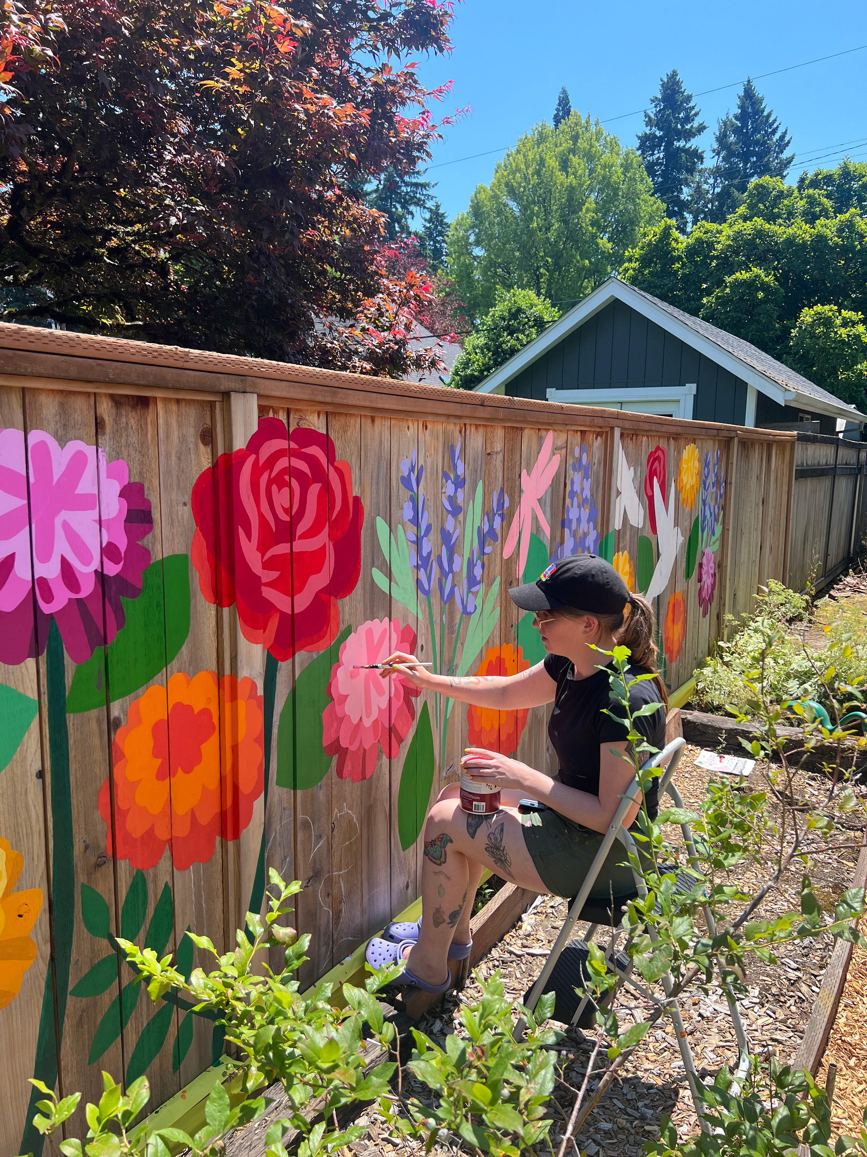 Muralist Lauren Blair painting a wildflower on a fence 